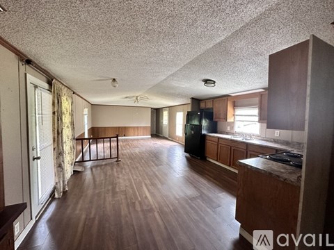 A spacious living room with wood flooring and a kitchen area with a stove top oven.