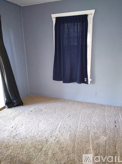A room with a carpeted floor and a window with a dark curtain.