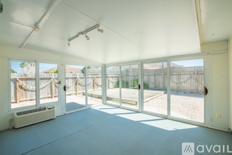 A room with a white ceiling and a large window with a view of a fence and trees.