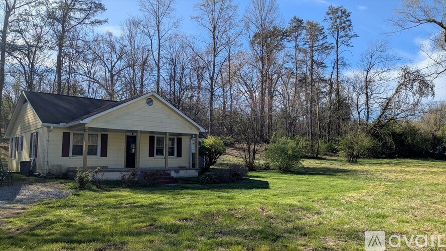 A yellow house with a black roof is surrounded by trees.