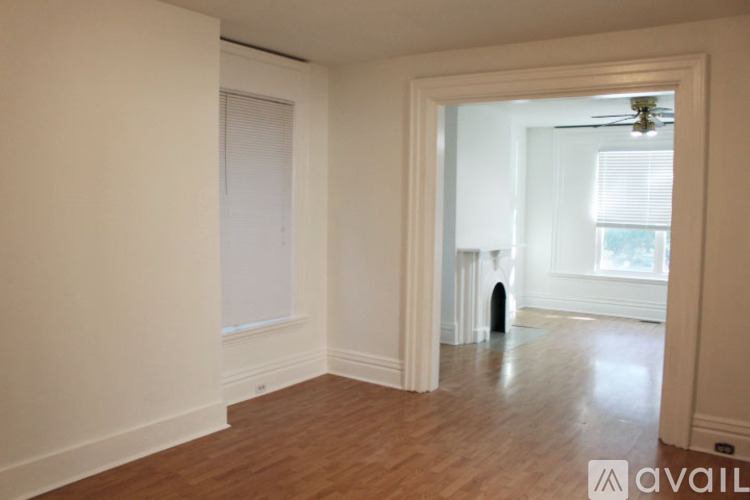 A room with wooden floors and white walls, with a doorway leading to another room.