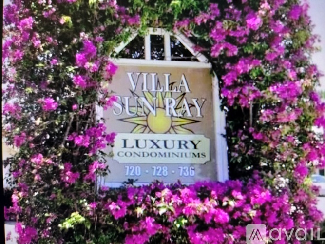 A sign for Villa Sunray Luxury Condominiums surrounded by purple flowers.