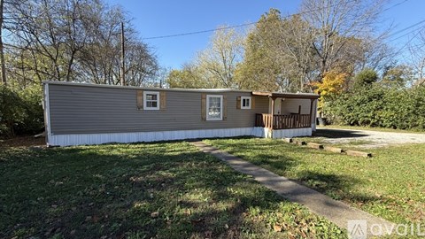 A mobile home is for sale in a grassy area with trees in the background.