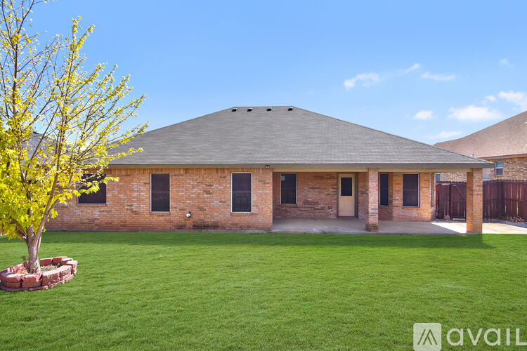A large, open grassy area in front of a building with a tree in a planter.
