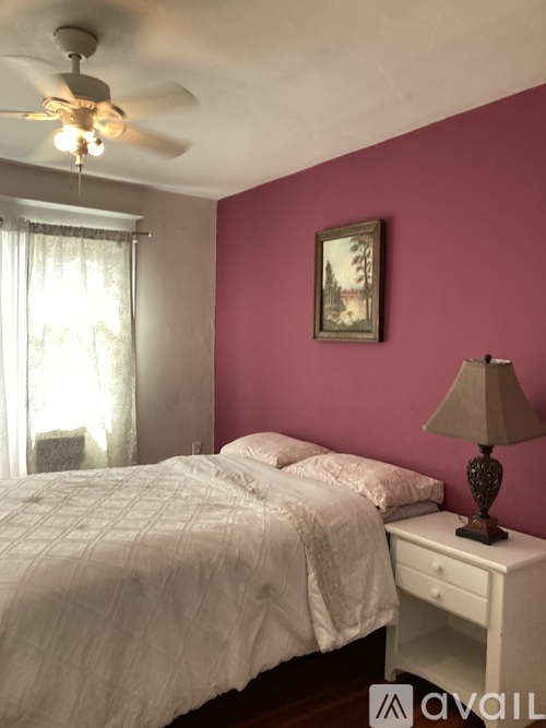 A bedroom with a bed, a ceiling fan, and a nightstand with a lamp.
