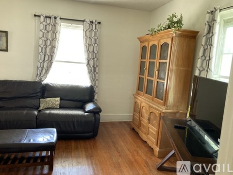 A living room with a black leather couch and wooden furniture.