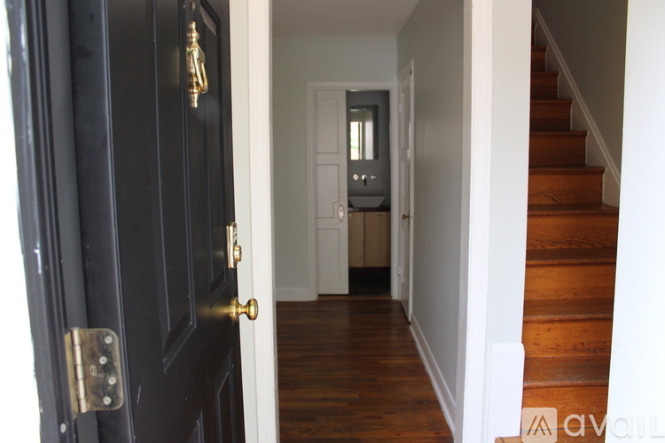 A black door with a gold handle is open to a hallway with a staircase.