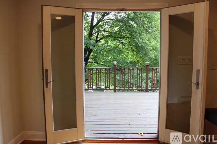 A glass door opens to a deck with a railing and trees.
