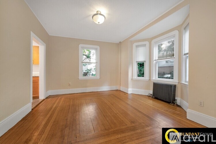 A room with wooden floors and a window showing trees outside.