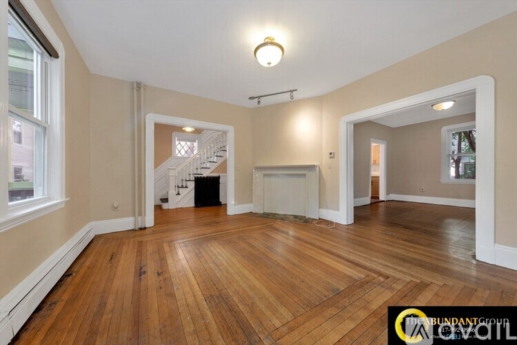 A spacious room with wooden floors and a staircase in the background.