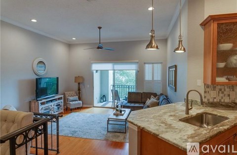 A living room with a television, a couch, a chair, a table, and a kitchen area with a sink and a counter.