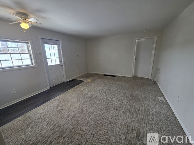 A room with a carpeted floor, a ceiling fan, and two doors.