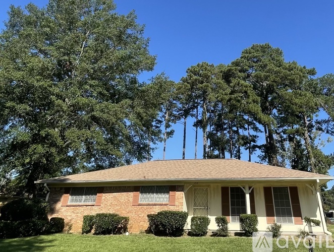 A house with a red brick exterior and a brown roof surrounded by green trees.
