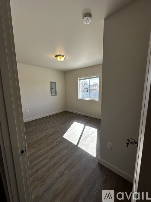 A room with wooden flooring and a window letting in sunlight.