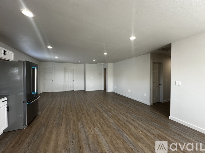 A spacious room with wooden flooring and a refrigerator on the left side.