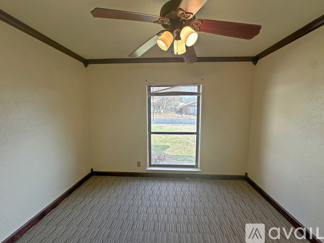 A room with a ceiling fan and a window overlooking a grassy area.