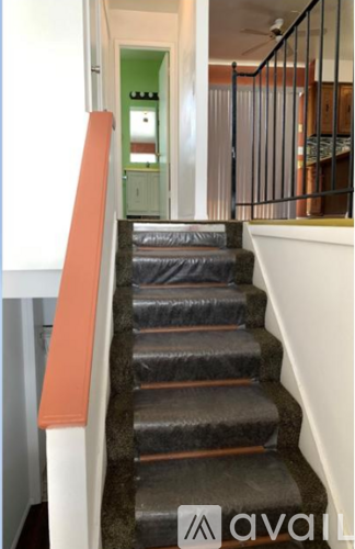 A staircase with a black carpeted runner and orange handrail.