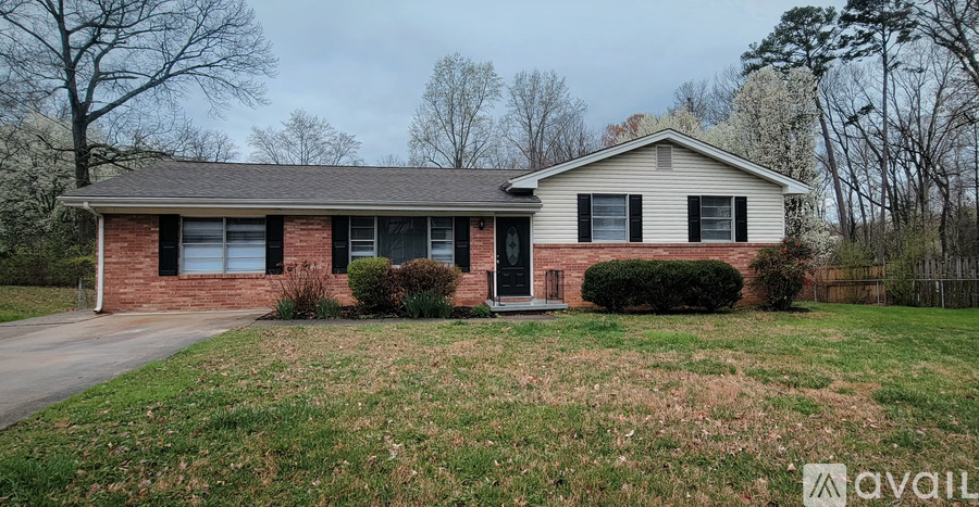 A house with a brick facade and a grey roof is surrounded by a grassy lawn and trees.