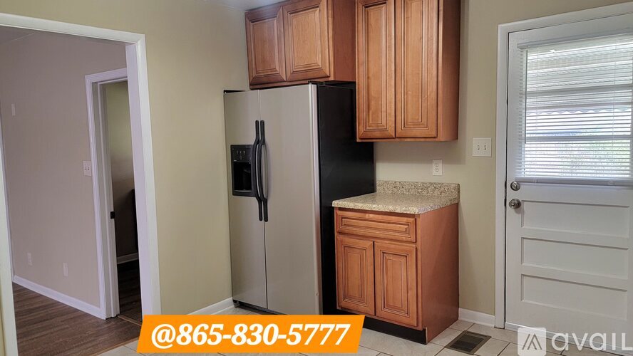 A kitchen with a black refrigerator, wooden cabinets, and a door leading to another room.