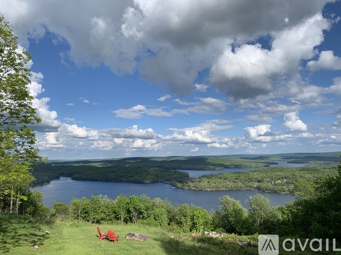 A red chair is on a grassy hill overlooking a lake.