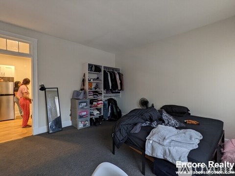 A bedroom with a bed, a wardrobe, and a person standing by the door.