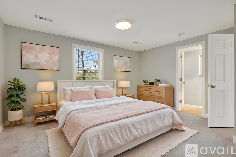 A bedroom with a large bed, two lamps, and a potted plant.