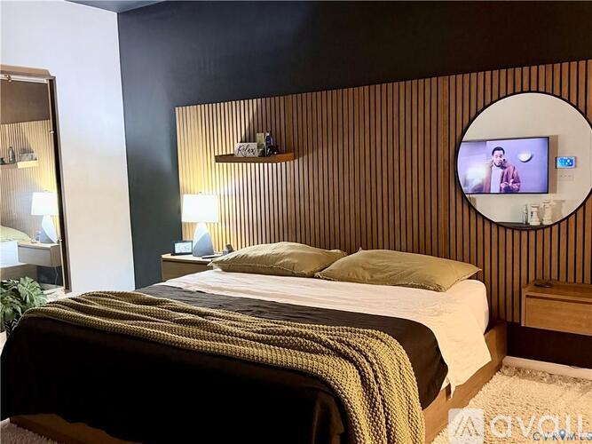 A bedroom with a bed, nightstand, and a round mirror on the wall.