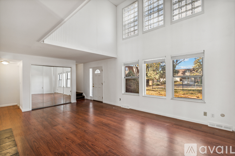 A spacious room with wood flooring and three windows with pictures on the wall.