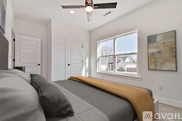 A bedroom with a bed, pillows, a ceiling fan, and a window with a view of a house outside.
