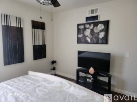 A bedroom with a bed, a television, and a painting on the wall.