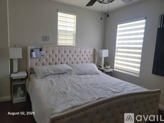 A bedroom with a large bed, a ceiling fan, and two windows with blinds.