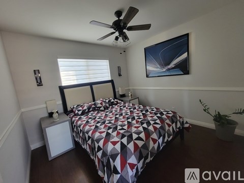 A bedroom with a large bed, a ceiling fan, and two windows with blinds.