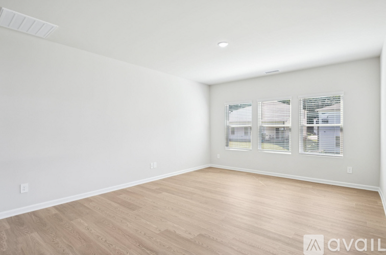 A spacious room with wooden flooring and a window with blinds.
