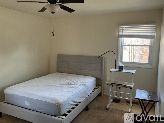 A bedroom with a bed, a fan, and a small table with a lamp on it.