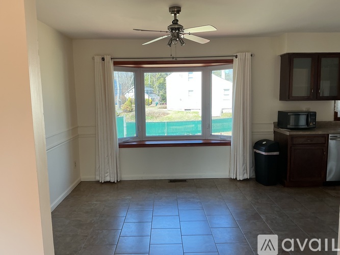 A room with a ceiling fan and a window overlooking a green area.