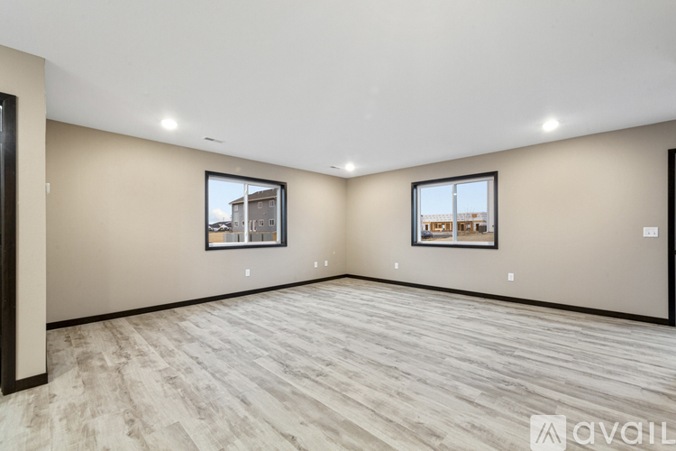 A spacious room with light wood flooring and two windows.