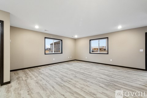 A spacious room with light wood flooring and two windows.