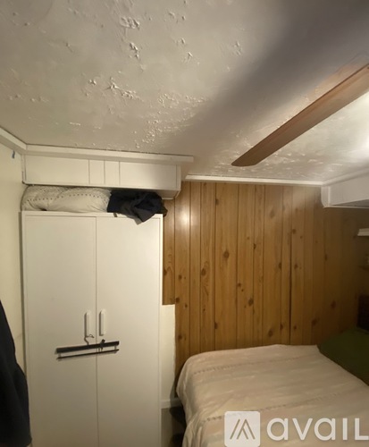 A small bedroom with a bed, wooden walls, and a white door.