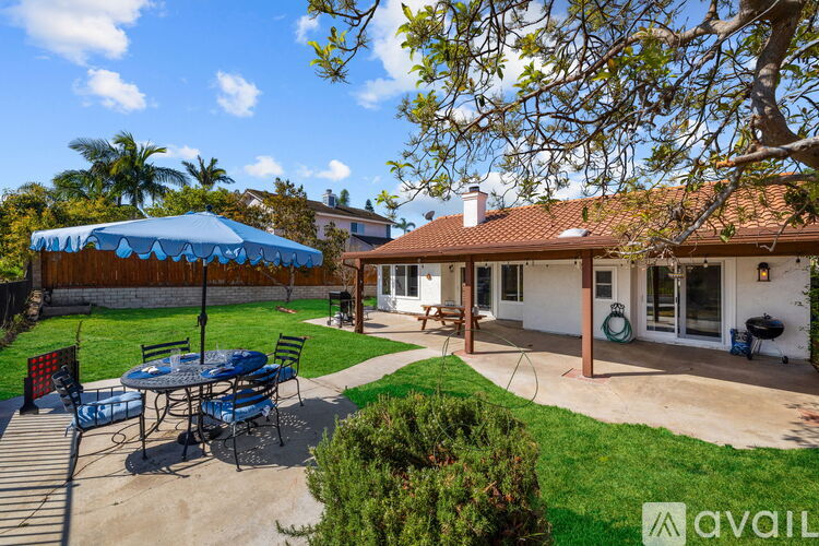 A patio with a table and chairs is surrounded by a green lawn and trees.