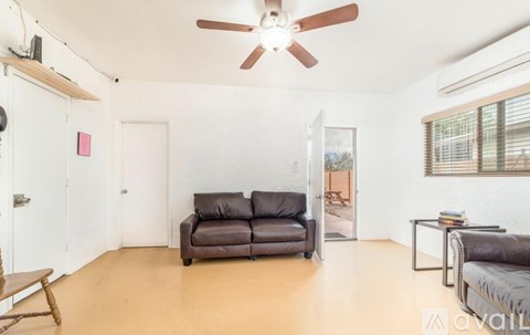 A living room with a brown leather couch and a ceiling fan.