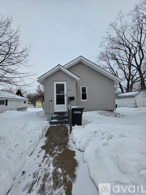 A house with a black trash bin in front of it.