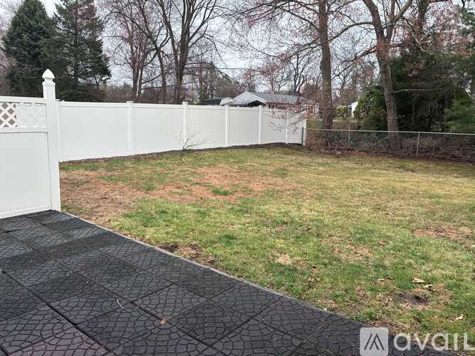 A white picket fence separates a driveway from a grassy area.