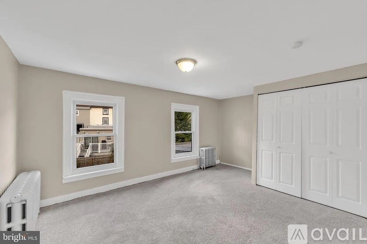 A spacious room with a window, a radiator, and a closed white door.