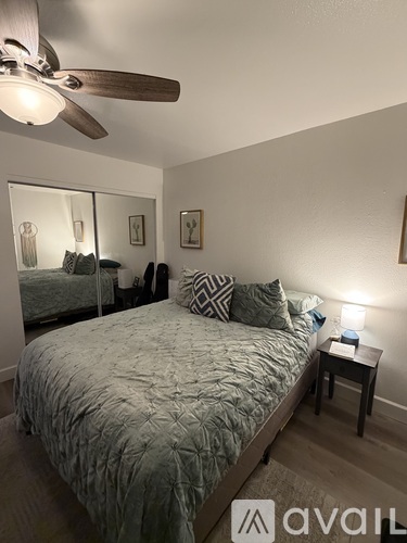 A bedroom with a bed, a ceiling fan, and a nightstand with a lamp.