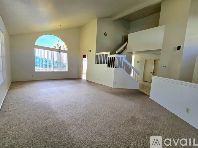 A spacious living room with a carpeted floor and a staircase leading to the upper level.