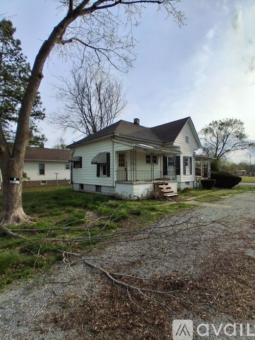 A white house with a porch and a tree in front.