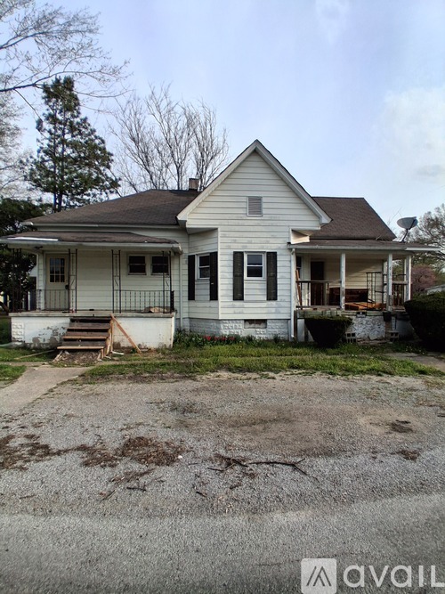 A white house with a brown roof and a gravel driveway in front.