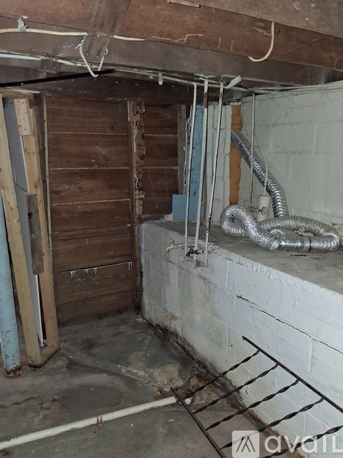 A dirty crawlspace with a wooden door and a metal pipe.