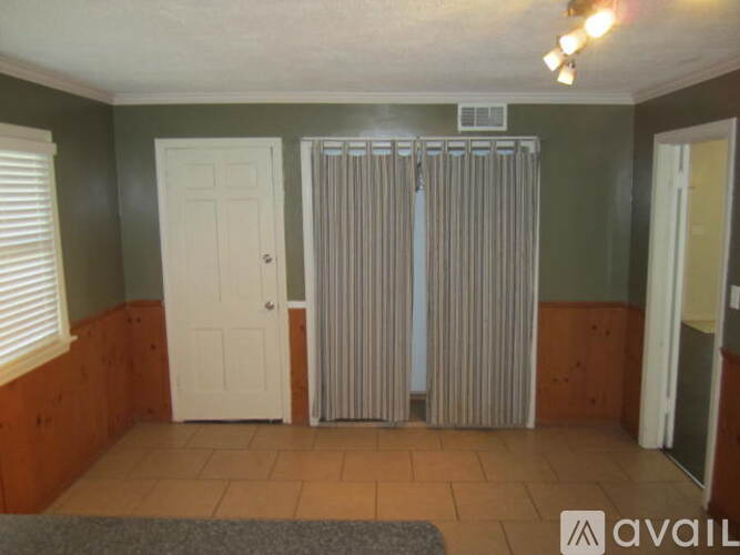 A room with a white door, a window with blinds, and a radiator.