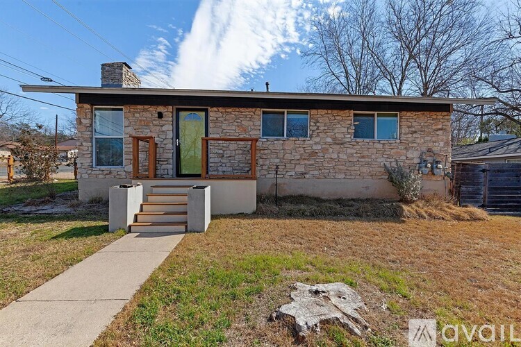 A house with a stone facade and a green door is surrounded by a grassy area.